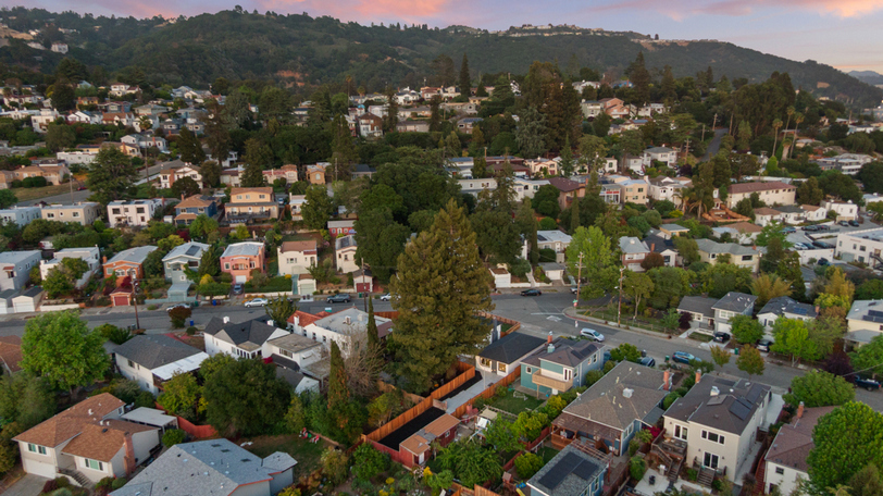 Aerial neighborhood view showcasing the property's setting among tree-lined streets and hillside surroundings.