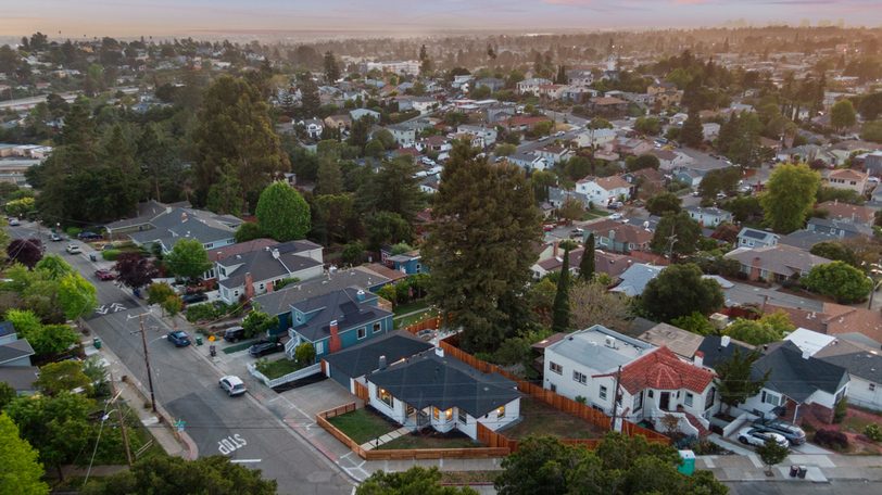 Aerial sunset view highlighting the corner-lot location, fenced yard, and surrounding residential neighborhood.