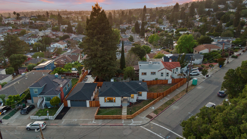 Aerial view showcasing the corner-lot setting, detached garage, expansive yard, and mature trees in a charming residential neighborhood.