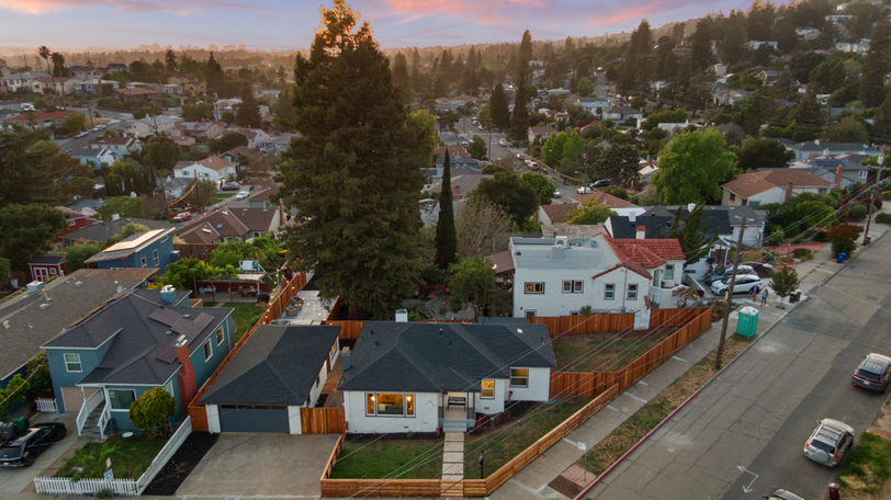 Aerial twilight view showcasing the corner-lot location, detached garage, expansive fenced yard, and towering mature trees.