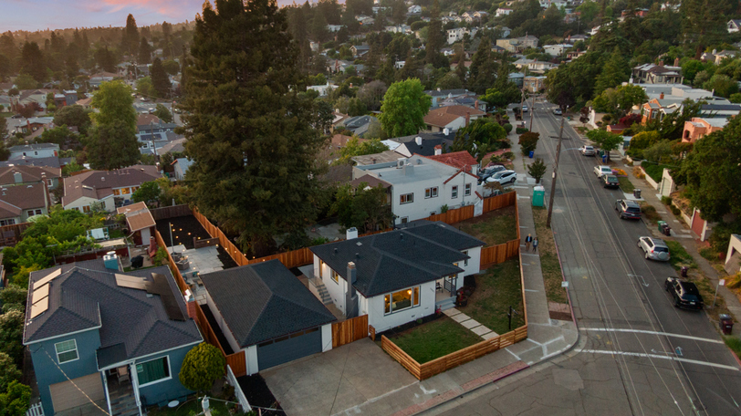 Aerial view highlighting the corner-lot location, detached garage, fenced yard, and mature trees in a desirable hillside neighborhood.