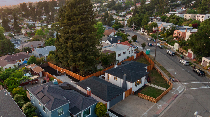 Aerial view highlighting the corner-lot setting, detached garage, expansive fenced yard, and mature trees that create a private outdoor retreat.