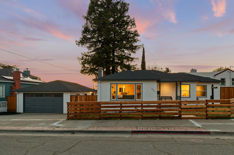 Twilight exterior showcasing the charming front façade, detached garage, and striking mature redwood backdrop.